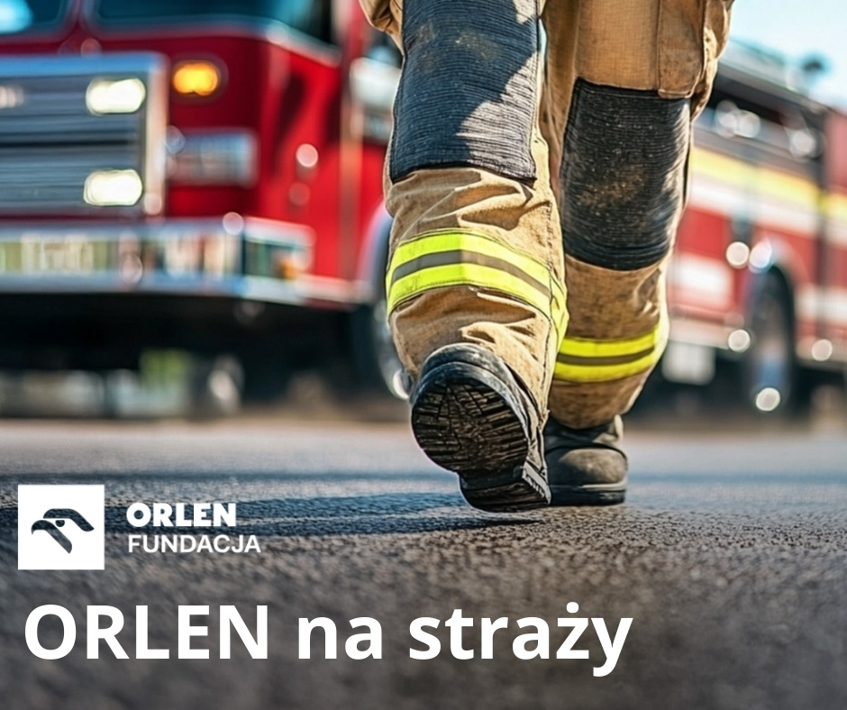 Zbliżenie na nogi strażaka w stroju ochronnym z odblaskowymi paskami, idącego po asfalcie. W tle czerwony wóz strażacki. Na dole logo Fundacji ORLEN i napis „ORLEN na straży